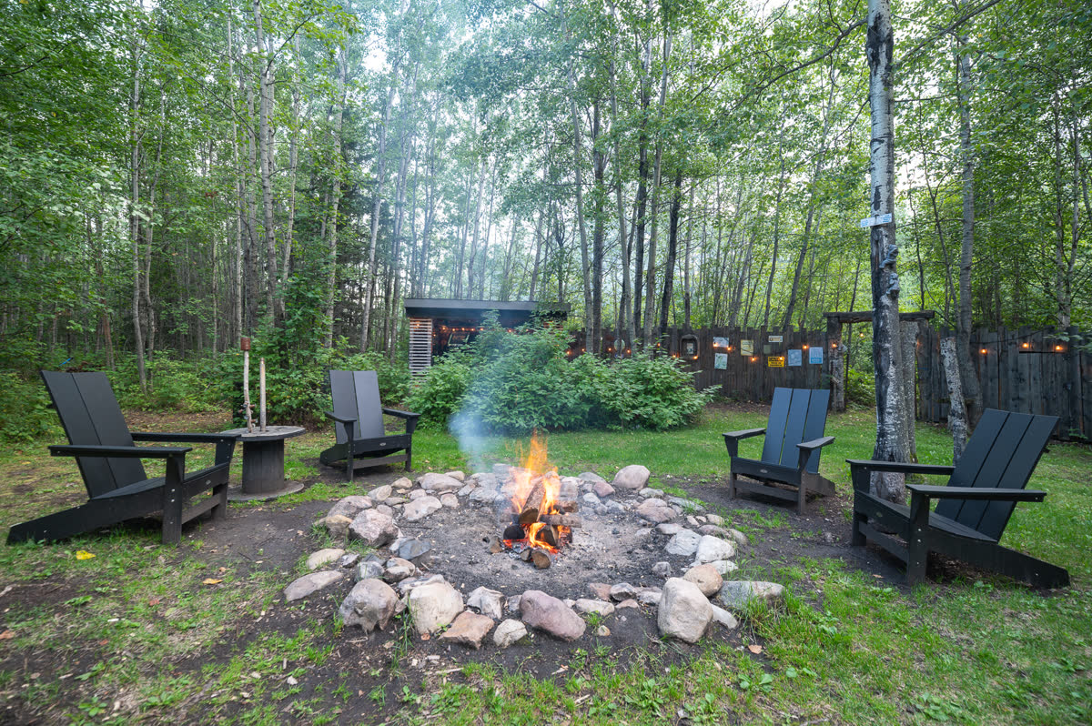 A firepit burning in a clearing ringed with Adirondack chairs