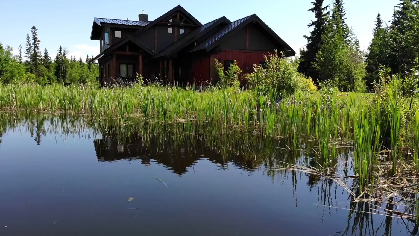 The lodge mirrored in the pond, reeds along the near bank