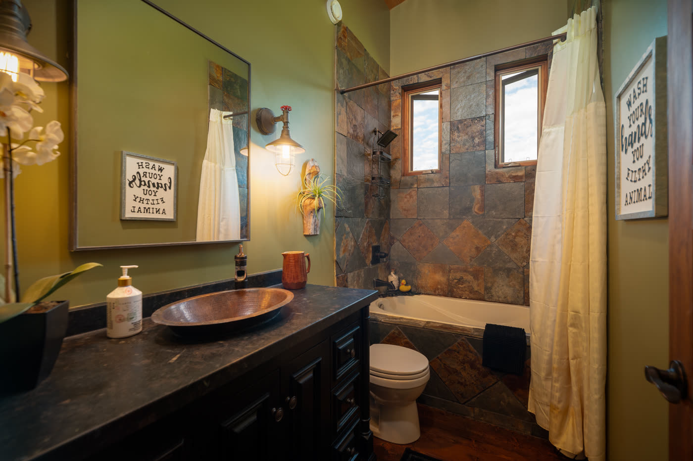 A bathroom with a copper vessel sink on a dark vanity and a slate wall