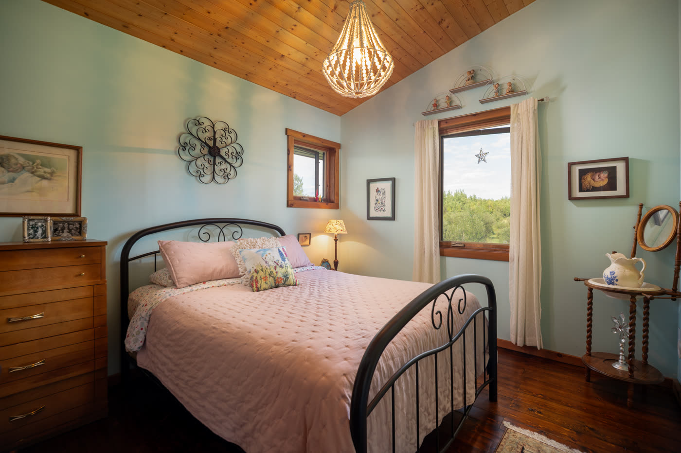 A bedroom with an iron bedstead and framed prints above the dresser