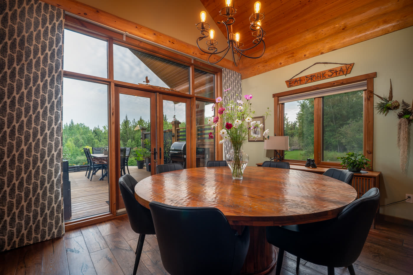 The dining table under a chandelier, glass doors opening onto the deck