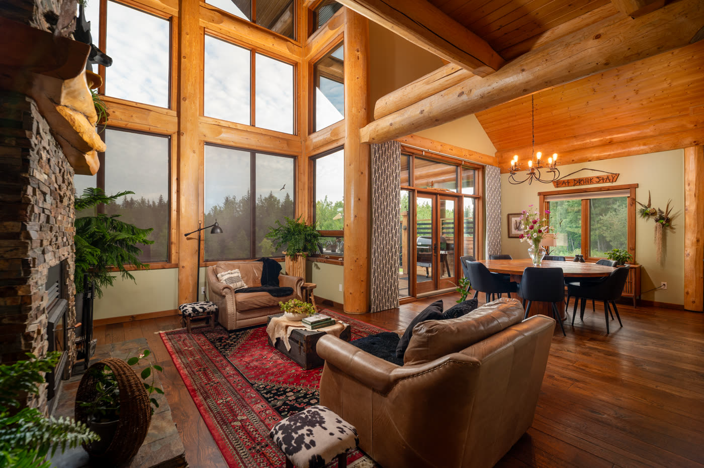The great room, its full-height windows framed in log posts, seating around a rug