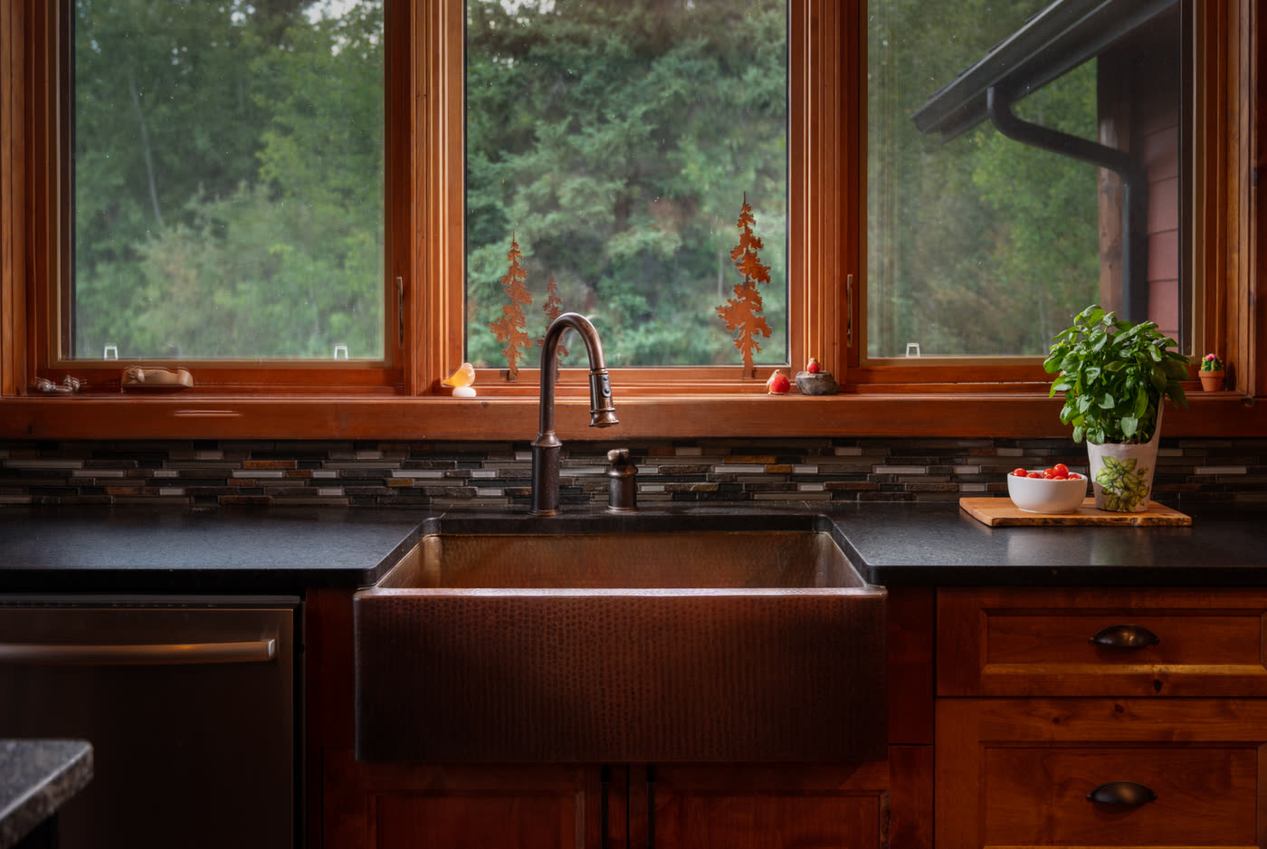 A copper farmhouse sink set under a window looking into the trees