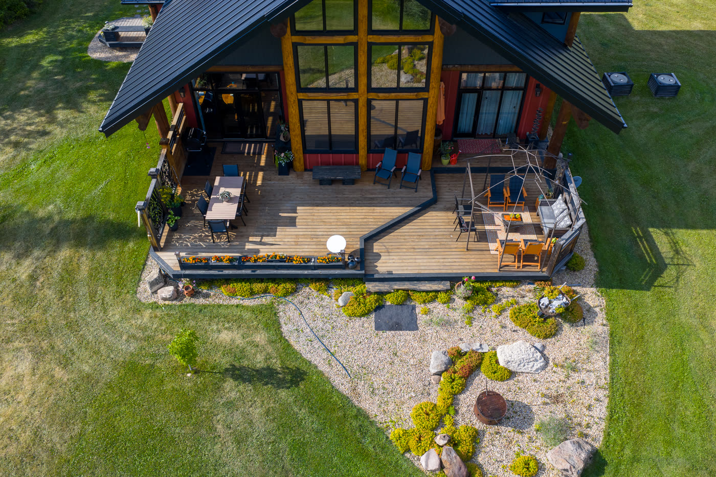 The lodge and its deck seen from above, patio furniture set out on the gravel
